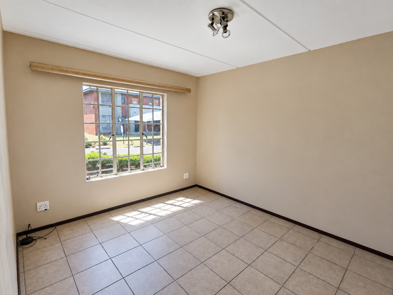A clean, empty bedroom featuring neutral wall paint, tiled flooring, and a window with security bars, providing a blank canvas for personalization.