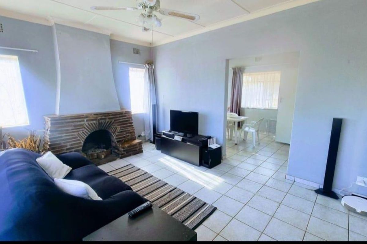 A living room featuring a traditional brick fireplace, tiled flooring, and a ceiling fan, with an adjacent dining area visible through the doorway.