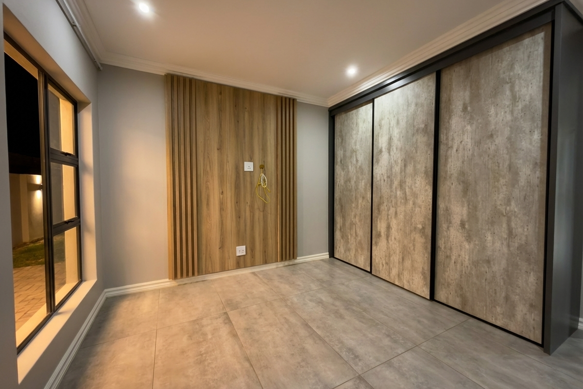 A modern bedroom featuring large built-in sliding door wardrobes, decorative timber wall paneling, recessed downlighting, and large format floor tiles.