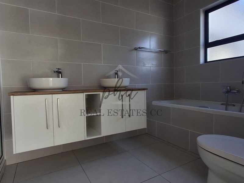 Modern bathroom featuring a double vanity with vessel sinks, a built-in bathtub, a separate shower enclosure, and neutral floor-to-ceiling wall tiles.