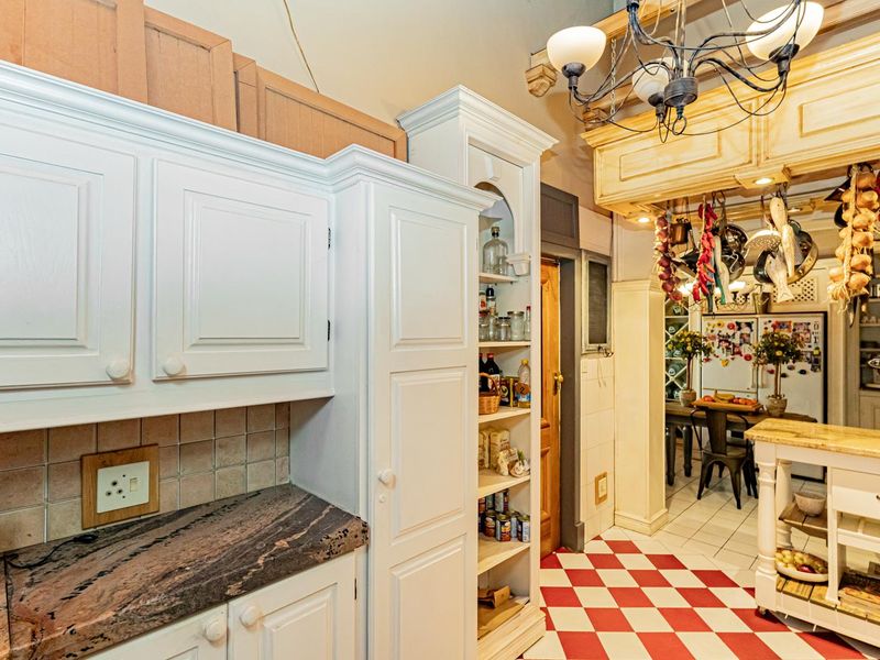 A traditional kitchen featuring white cabinetry, stone countertops, a tiled backsplash, and distinctive red and white checkerboard flooring.