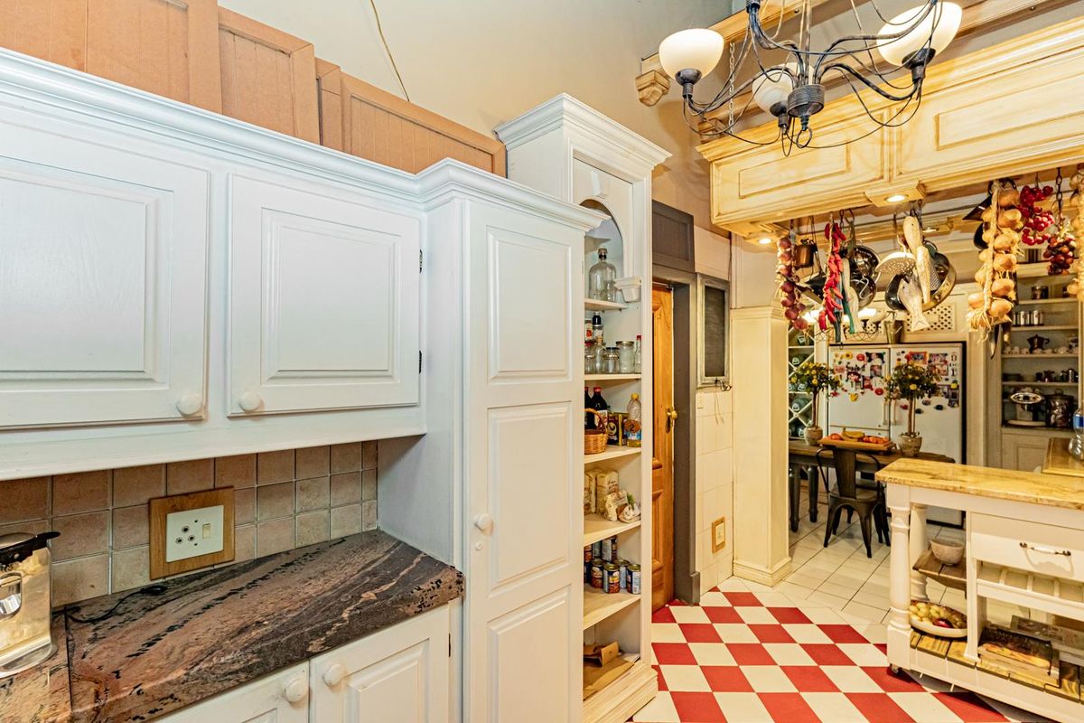 A traditional kitchen featuring white cabinetry, stone countertops, a tiled backsplash, and distinctive red and white checkerboard flooring.