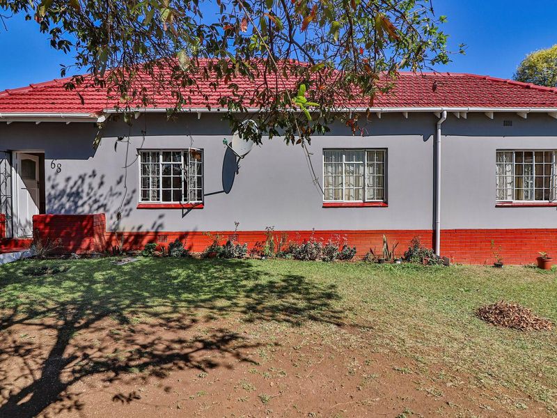 Front elevation of a single-story house featuring a red tiled roof, grey painted walls with a red brick base, and security bars on windows.
