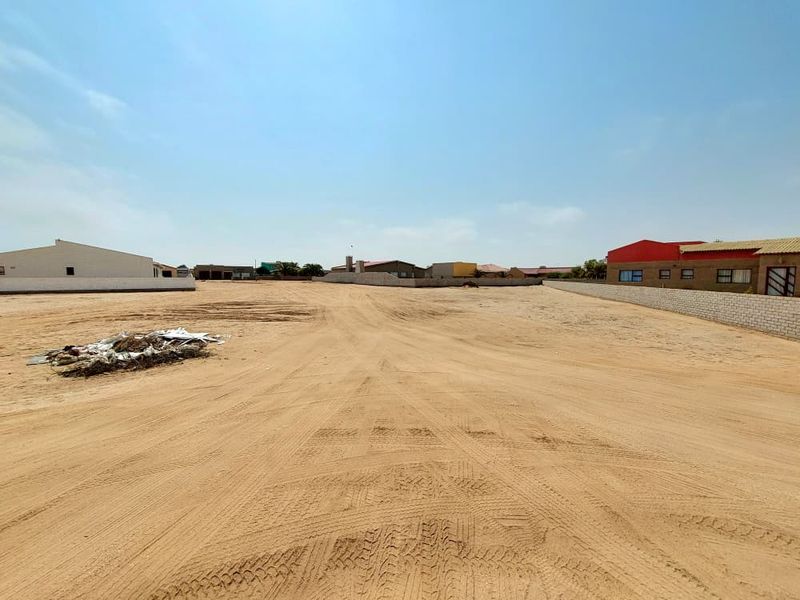 A vacant residential plot of land featuring sandy ground and perimeter boundary walls, situated in a developed neighborhood.