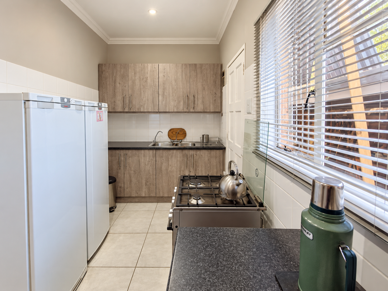 A functional scullery featuring wood-look cabinetry, laminate countertops, a stainless steel sink, and a gas hob, complemented by tiled splashbacks and flooring.