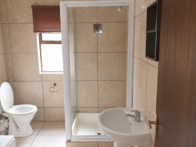 A functional bathroom featuring a pedestal basin, shower enclosure, and toilet with neutral wall and floor tiling.