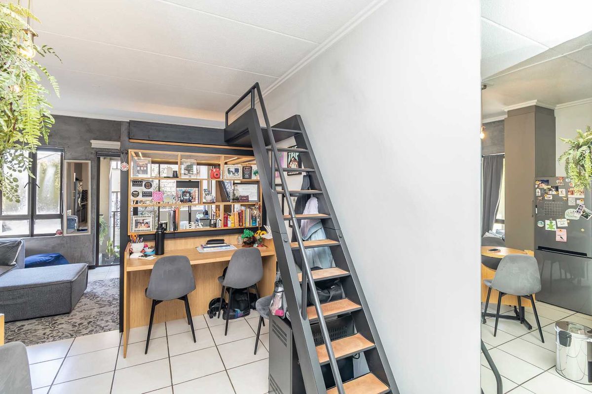 Open-plan living area featuring a built-in desk and shelving unit with a mezzanine staircase, tiled flooring, and access to a balcony.