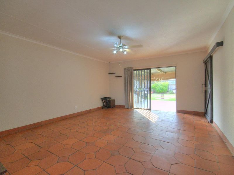 Spacious living area featuring terracotta floor tiles, a ceiling fan, and a sliding door providing direct access to the outdoor patio and garden.