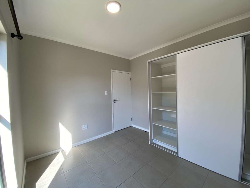 A clean, neutral-toned bedroom featuring tiled flooring and a large built-in sliding door wardrobe with integrated shelving.