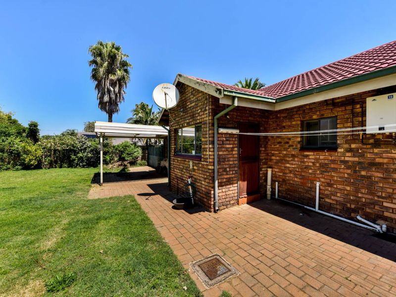 Rear view of the property featuring a brick facade, paved patio area, carport, and established garden space.