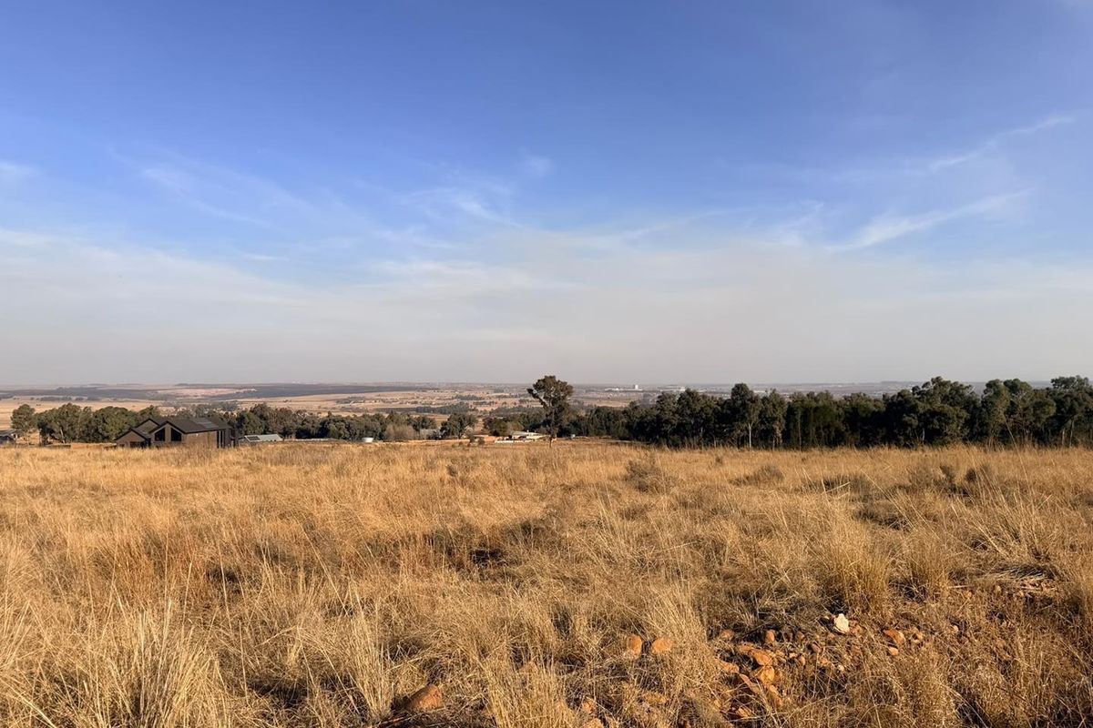 Expansive view over open, undeveloped residential land featuring dry grass and distant tree lines under a clear blue sky.