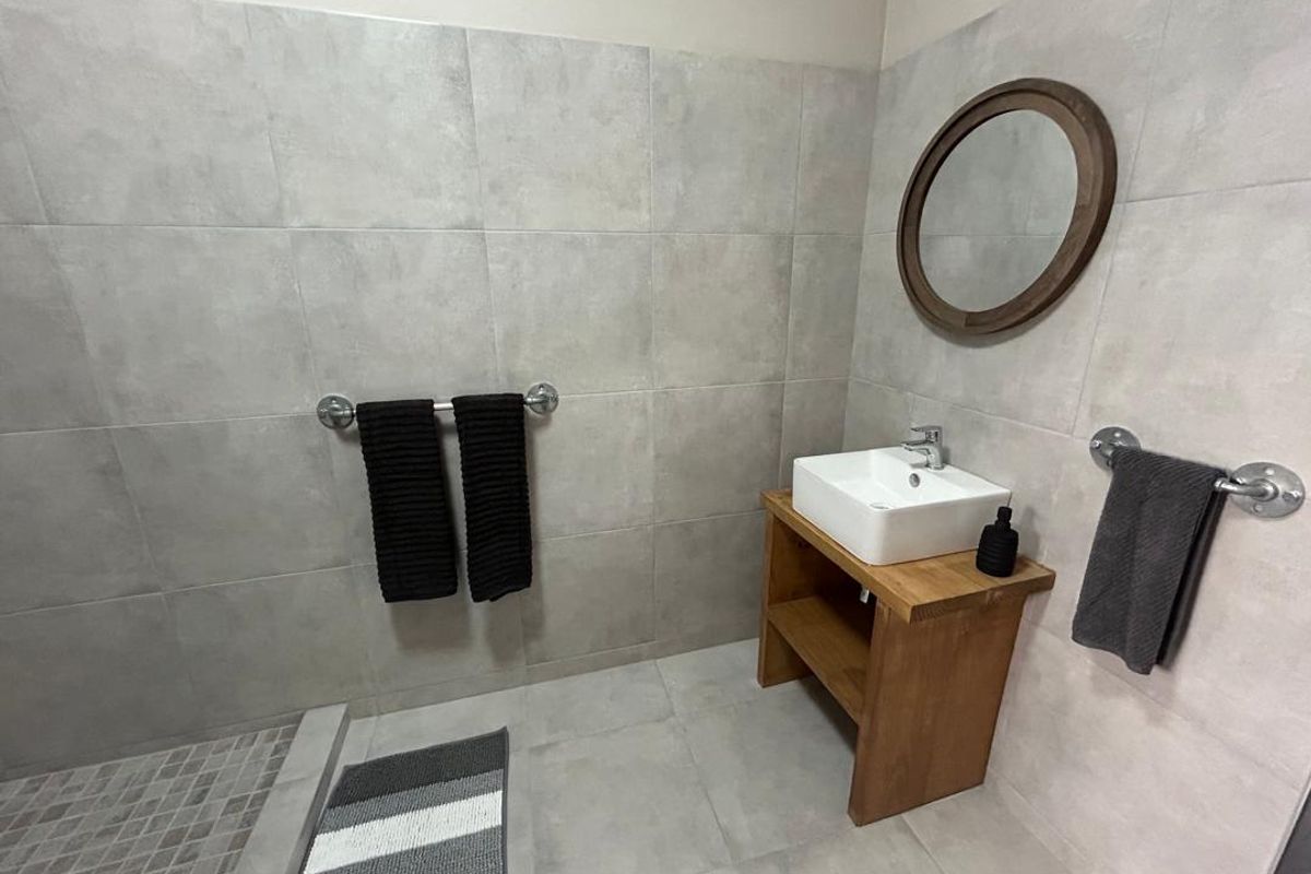 Modern bathroom featuring large format grey wall and floor tiles, a vessel sink on a wooden vanity, and a walk-in shower area.