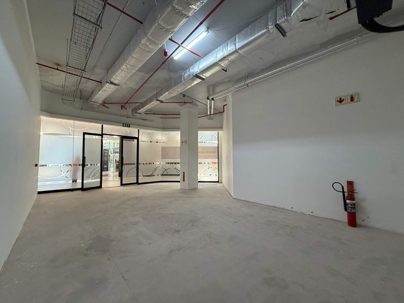 An open-plan retail space featuring exposed industrial ceiling ducting, concrete flooring, and glass partition walls, suitable for a variety of commercial uses.