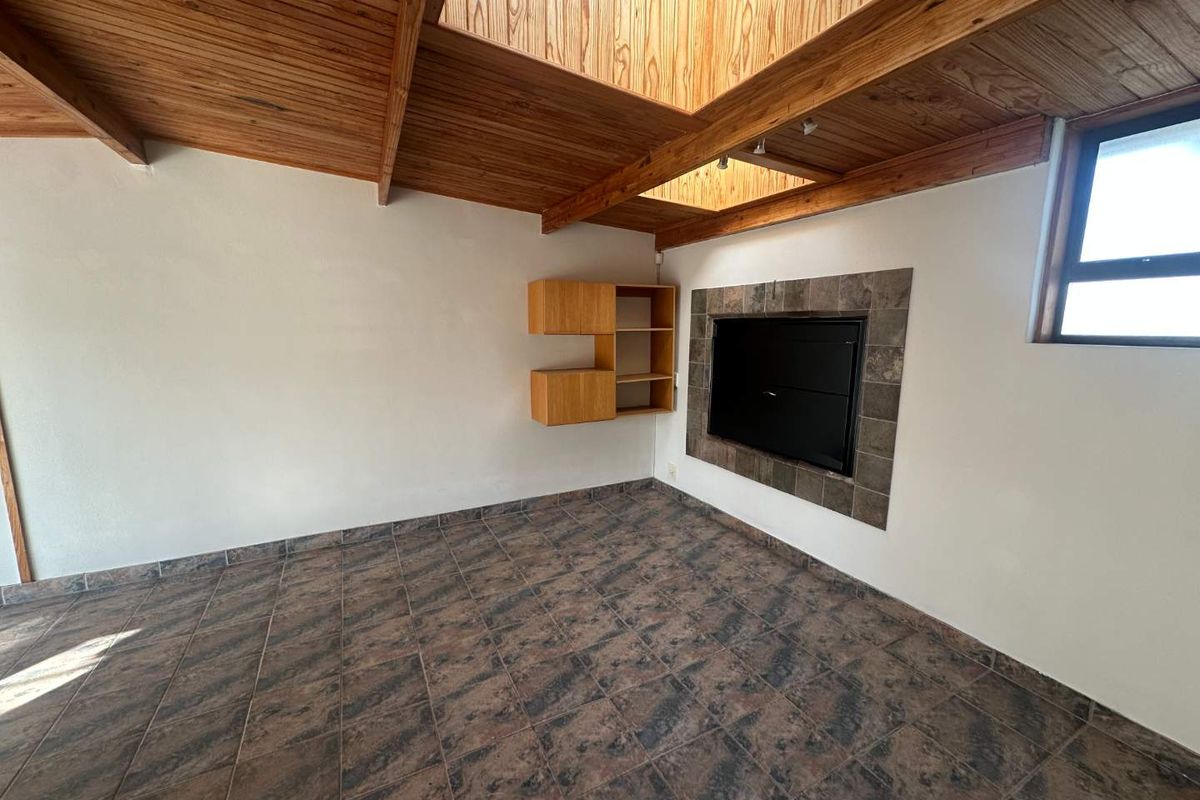 Spacious living room featuring a vaulted timber ceiling with a skylight, tiled flooring, and a built-in fireplace with stone surround.