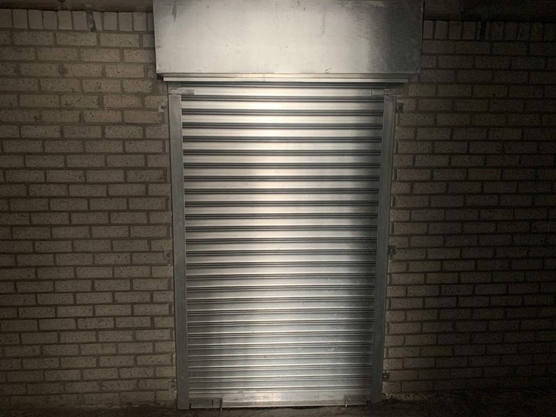 A secure utility space featuring a metal roller shutter door set within an exposed brick wall.