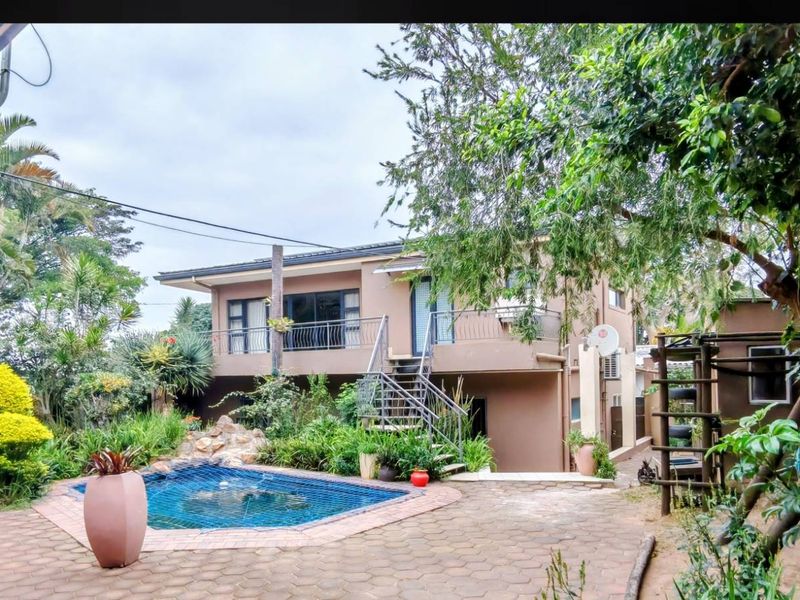 Rear exterior view of the house featuring a paved patio area, a swimming pool, and an external metal staircase leading to the upper balcony.