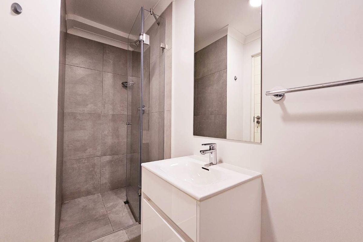 Modern bathroom featuring a glass-enclosed walk-in shower with grey tiling, a sleek vanity unit, and a wall-mounted mirror.