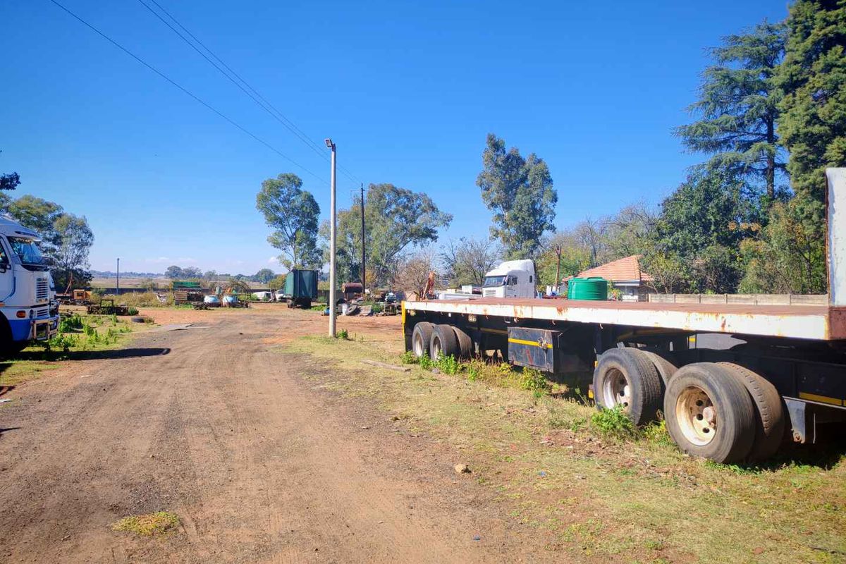 An expansive outdoor farm yard area featuring unpaved access paths, utility poles, and open space suitable for agricultural or industrial storage.