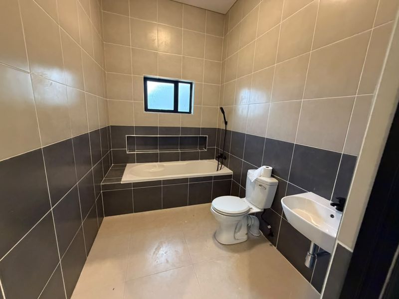 A clean, modern bathroom featuring a built-in bathtub with a recessed niche, a wall-mounted basin, and a toilet, finished with neutral two-tone wall tiling.