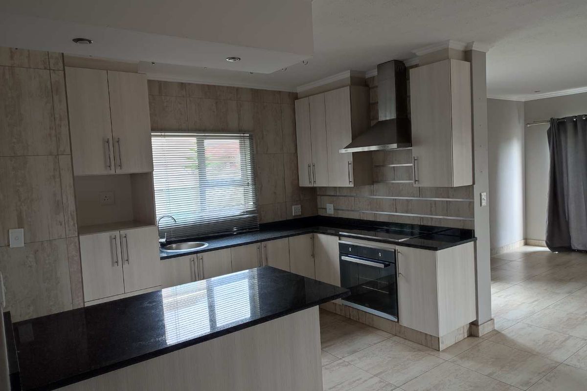 Modern kitchen featuring light wood cabinetry, granite countertops, a built-in oven, and a stainless steel extractor fan.