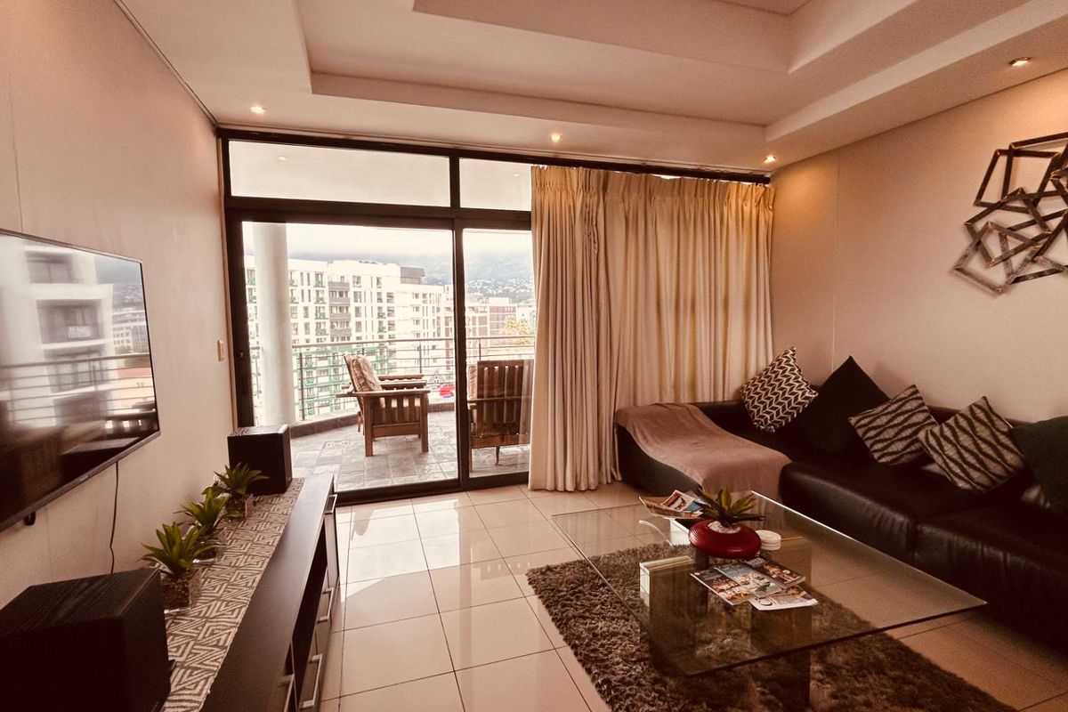 A well-maintained living room featuring tiled floors, recessed ceiling lighting, and large sliding glass doors that open onto a private balcony.
