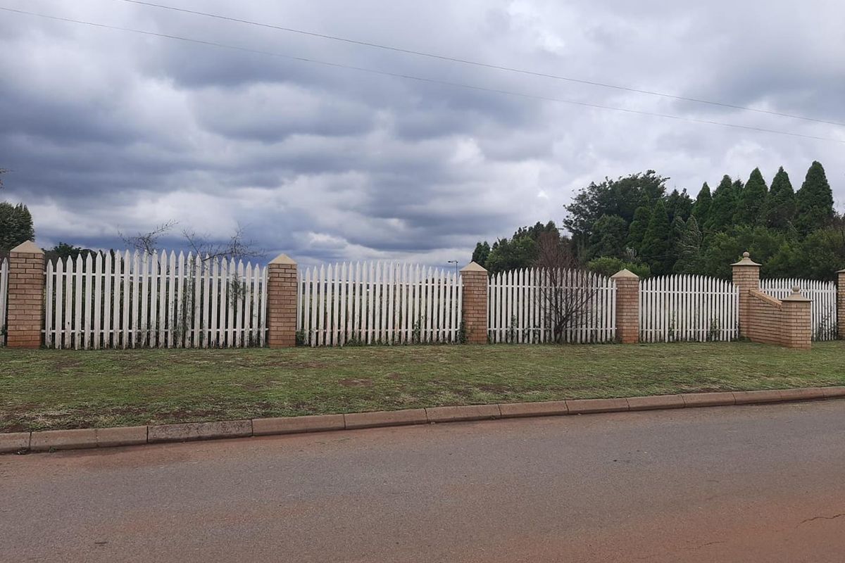 A view of the property boundary featuring a white picket fence supported by brick pillars along the street frontage.