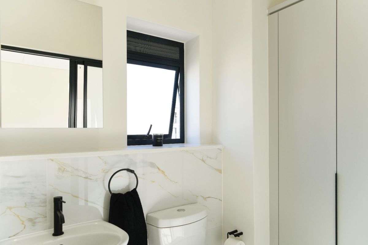 Modern bathroom featuring marble-look wall tiles, a sleek black basin mixer, built-in cabinetry, and a contemporary black-framed window.