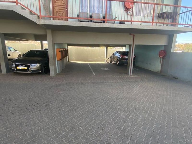 Covered ground-level parking area for a townhouse complex, featuring paved flooring, designated bays, and an overhead balcony with metal railings.
