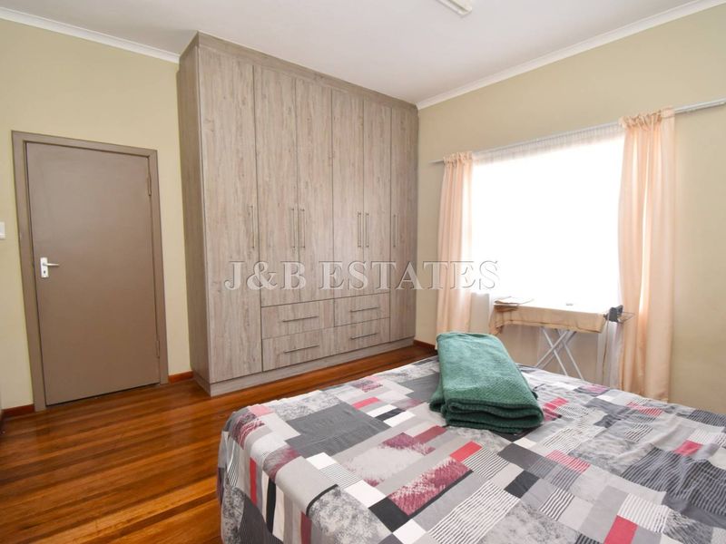 A well-maintained bedroom featuring polished timber flooring and extensive built-in cabinetry with a neutral color palette.