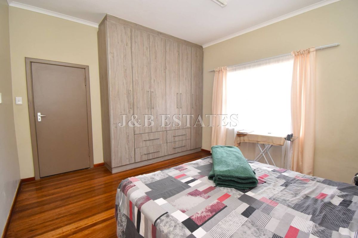 A well-maintained bedroom featuring polished timber flooring and extensive built-in cabinetry with a neutral color palette.