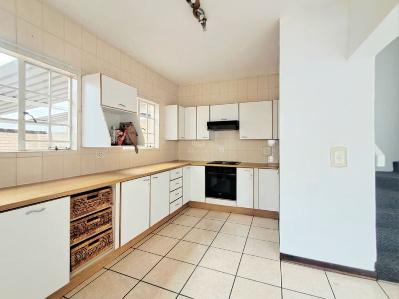 A functional kitchen featuring white built-in cabinetry, tiled splashbacks, a built-in oven with hob, and tiled flooring.