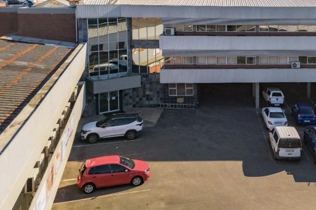 Aerial view of a commercial retail property featuring a multi-level building with metal roofing, stone facade accents, and an expansive asphalt parking lot.