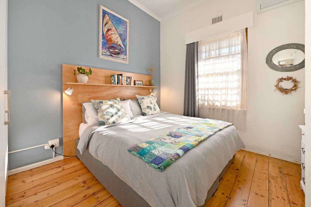 A cozy bedroom featuring polished timber flooring, a built-in wooden headboard, and an integrated air conditioning unit.