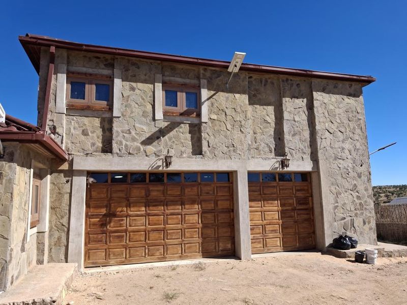 A double garage featuring stone-clad exterior walls and timber garage doors, complemented by exterior lighting and functional guttering.