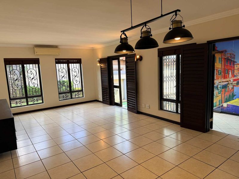 Spacious, light-filled living area featuring neutral tiled flooring, air conditioning, and secure window treatments with direct access to the exterior.