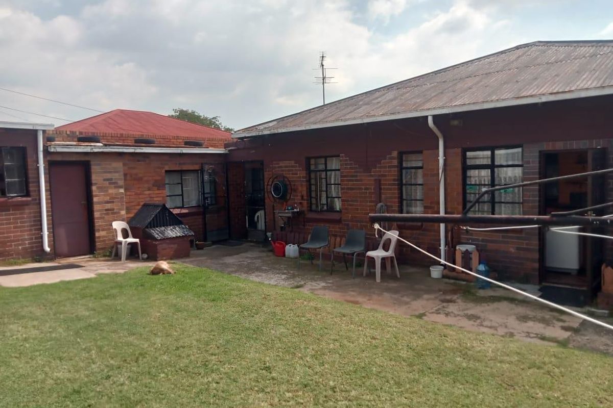 A view of the rear exterior of the house featuring a brick facade, corrugated metal roofing, and a paved patio area leading to the garden.