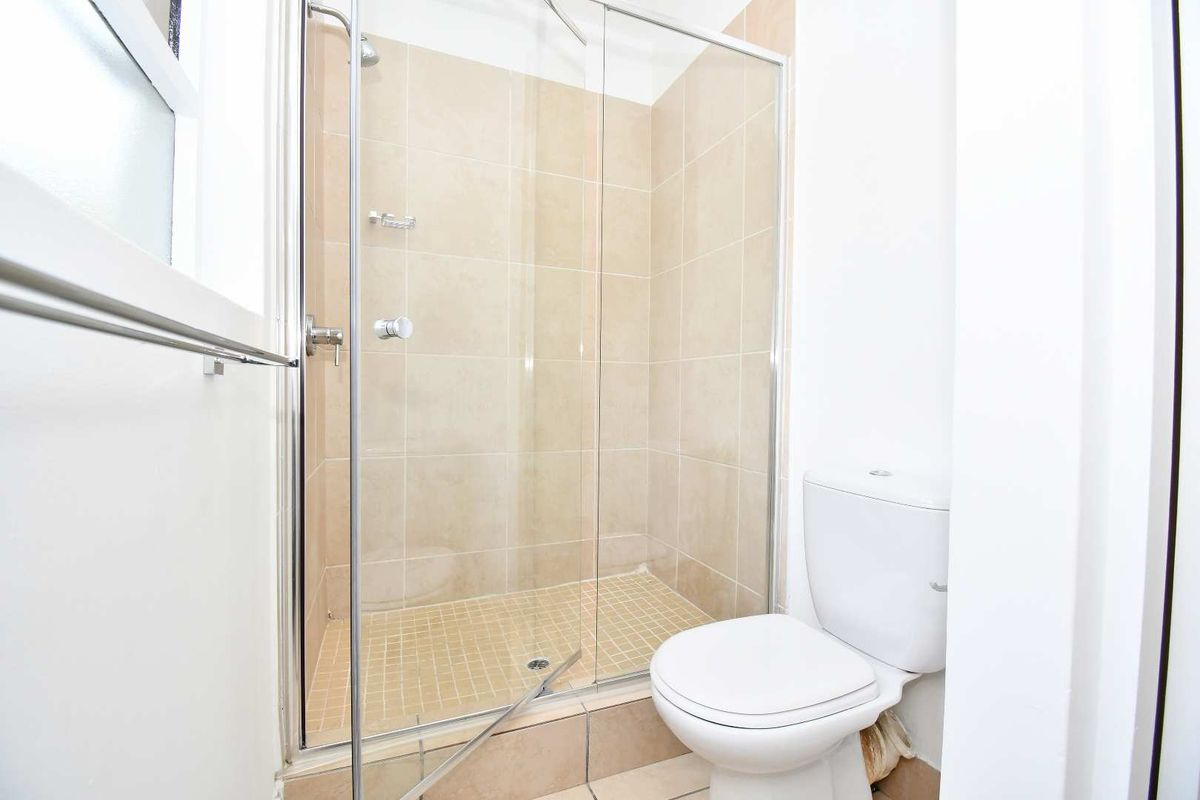 A functional bathroom featuring a glass-enclosed shower with beige tiling and a standard white toilet.