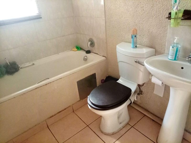 A functional bathroom featuring a standard bathtub, pedestal basin, and toilet with tiled flooring and partial wall tiling.
