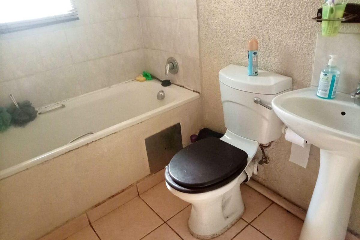 A functional bathroom featuring a standard bathtub, pedestal basin, and toilet with tiled flooring and partial wall tiling.