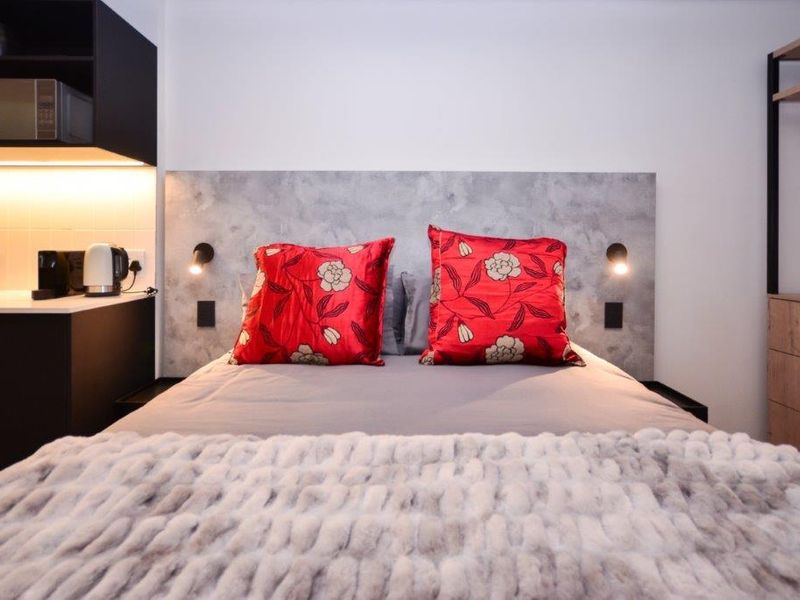 Modern bedroom featuring built-in cabinetry, integrated lighting, and a sleek headboard design with wall-mounted reading lights.