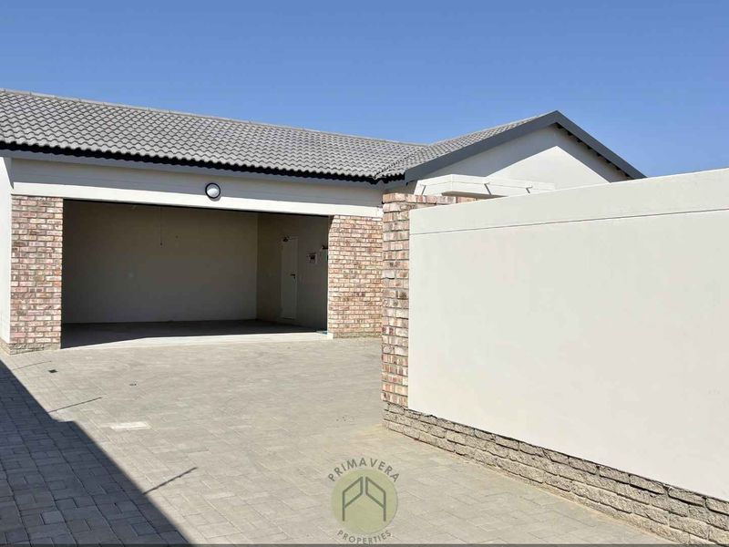 A modern residential exterior featuring a double garage, paved driveway, and a clean brick and plaster boundary wall with electric fencing.