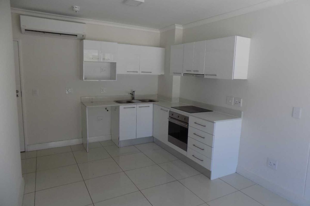 Modern kitchen featuring white cabinetry, stone countertops, integrated oven, hob, extractor fan, and tiled flooring.