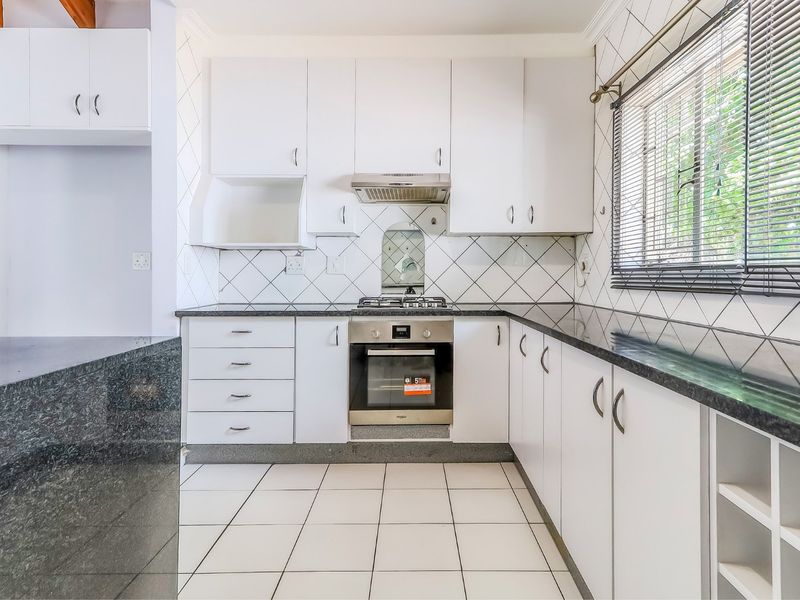 A clean, functional kitchen featuring white cabinetry, dark granite countertops, a gas hob, an electric oven, and a tiled backsplash.