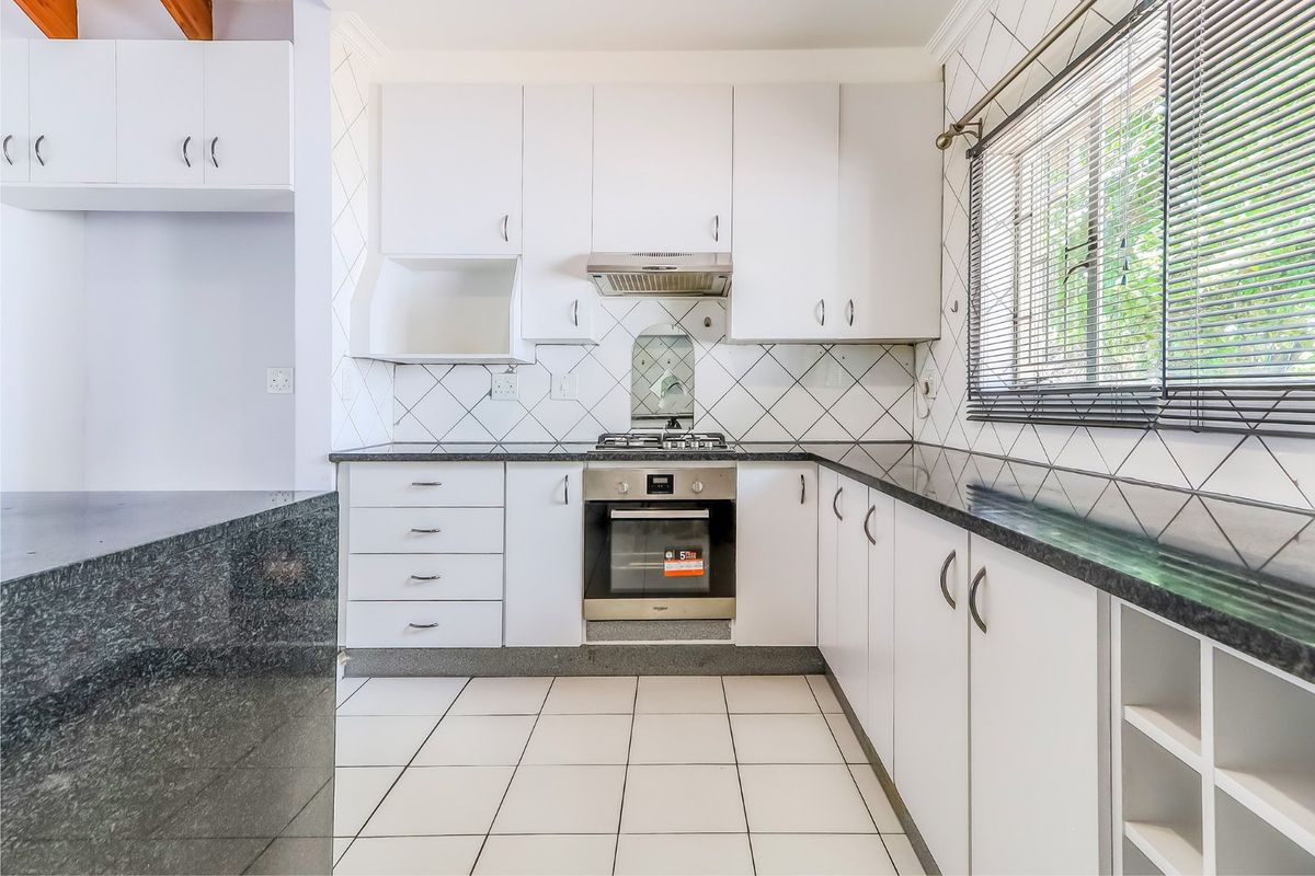 A clean, functional kitchen featuring white cabinetry, dark granite countertops, a gas hob, an electric oven, and a tiled backsplash.