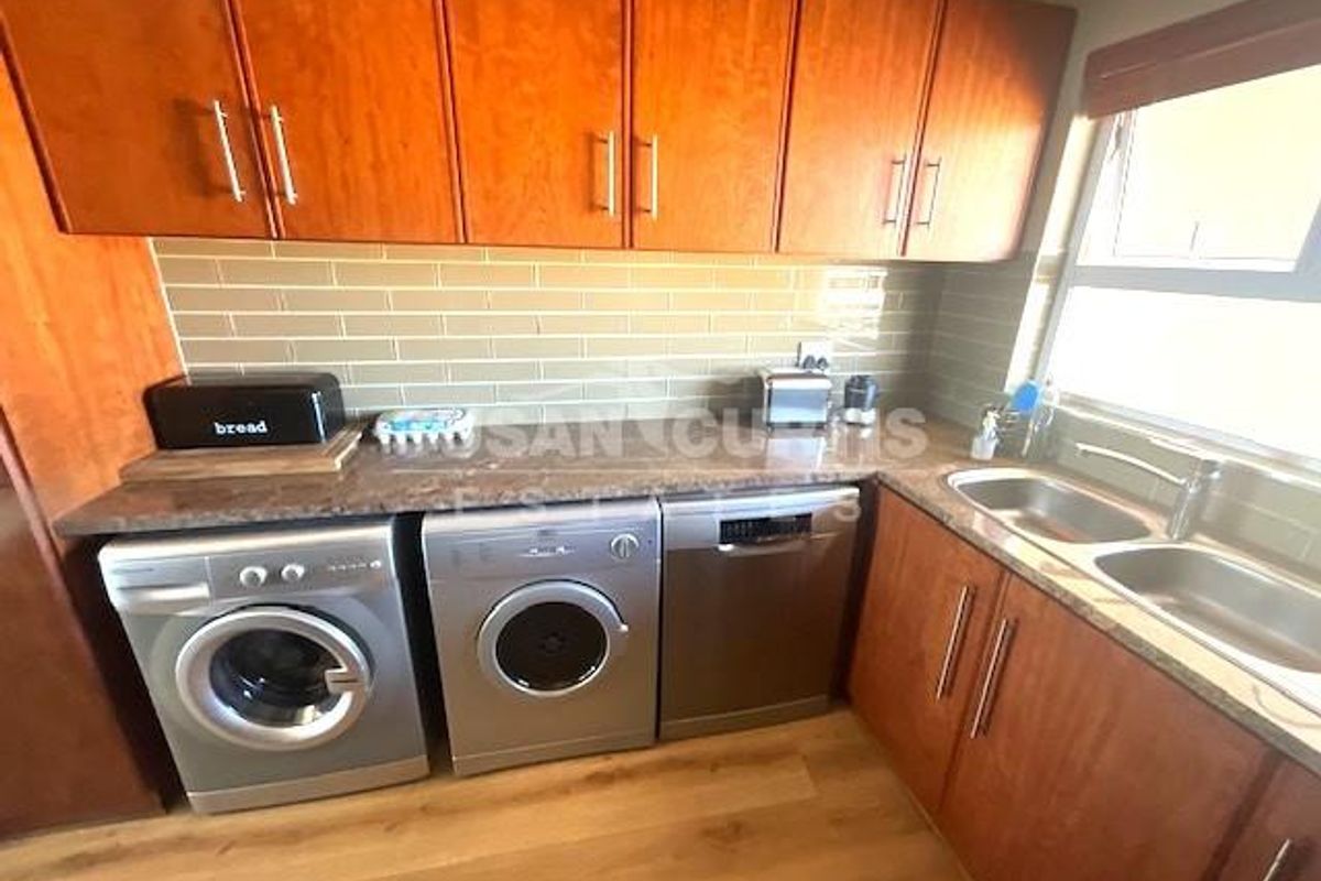 Functional kitchen featuring wooden cabinetry, granite countertops, double stainless steel sink, and integrated laundry appliance connections.