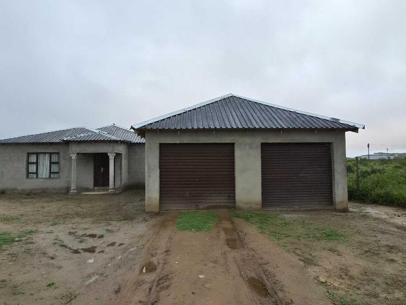 Front view of a single-story house featuring a double garage with roller shutter doors and an unfinished exterior facade.