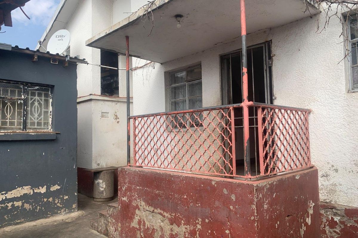 A weathered rear exterior area featuring a small covered porch with metal security railings and visible signs of paint deterioration on the building facade.