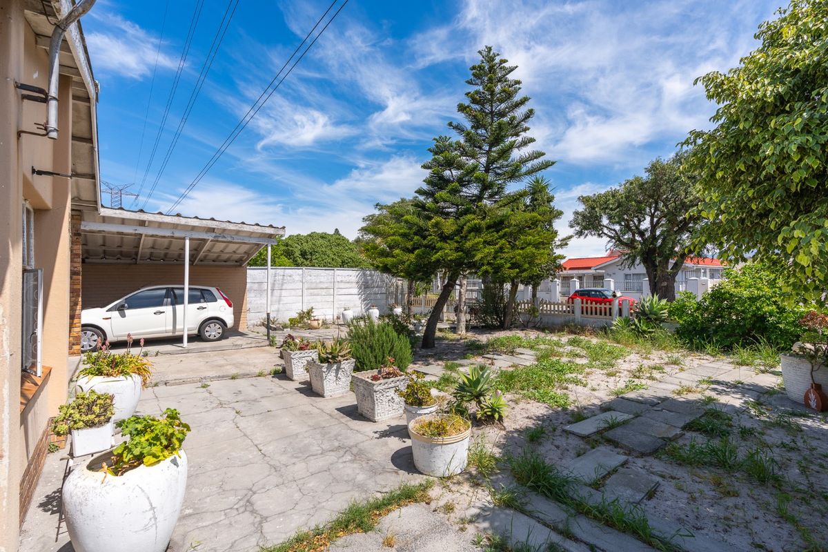 Rear exterior area featuring a carport, concrete paving with visible cracking, and a precast concrete boundary wall.
