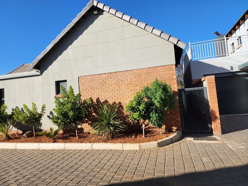 Exterior view of the townhouse featuring a brick and rendered facade, paved driveway, and a side garden area with a secure metal gate.