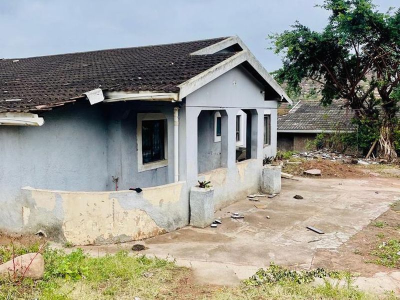 Rear view of a detached house showing a concrete patio area, tiled roof, and exterior walls requiring significant maintenance and repair.